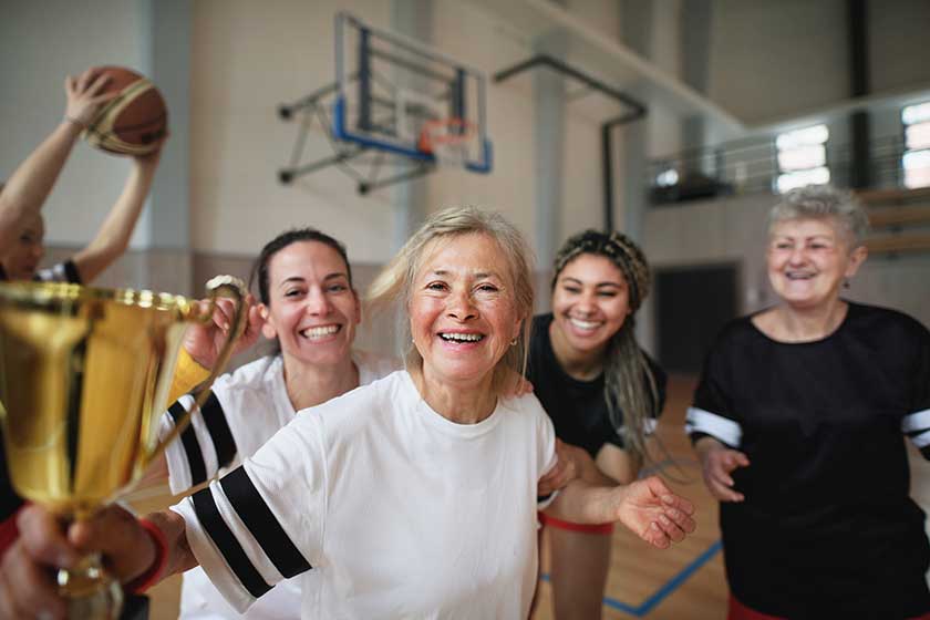 A group of young and old women, basketball team players, in gym with trophy celebrating victory.